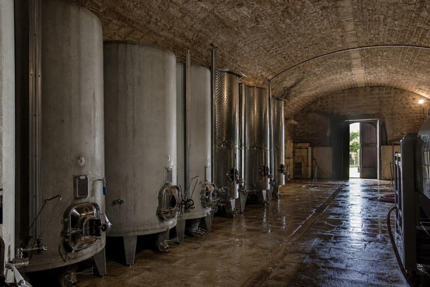 Une cave voûtée en pierre, des cuves béton et inox, la porte ouverte sur le jour